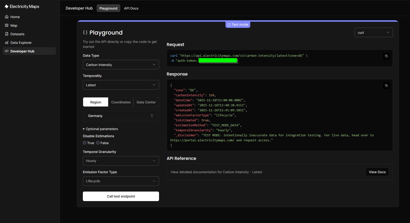 Electricity Maps API Playground interface showing a test API request for carbon intensity data. The left panel displays configuration options including Data Type set to "Carbon Intensity", Temporality set to "Latest", Region tab selected with "Germany" chosen, and optional parameters for emission factor type set to "Lifecycle" with hourly temporal granularity. The right panel shows a curl request to the carbon intensity API endpoint with an authentication token (highlighted in green), and below it a JSON response displaying Germany's current carbon intensity of 324 gCO2eq/kWh along with timestamps and a test mode disclaimer noting the data is intentionally inaccurate for integration testing purposes. The interface is in dark mode with blue accent highlighting indicating test mode is active.